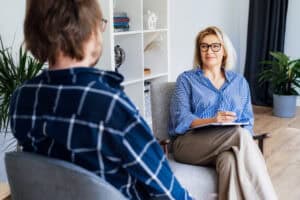 Two women, one is a therapist sitting in chairs talking and looking at eachother.