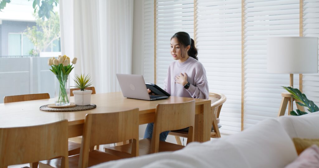 Woman sitting at dining room table talking to therapist on her laptop