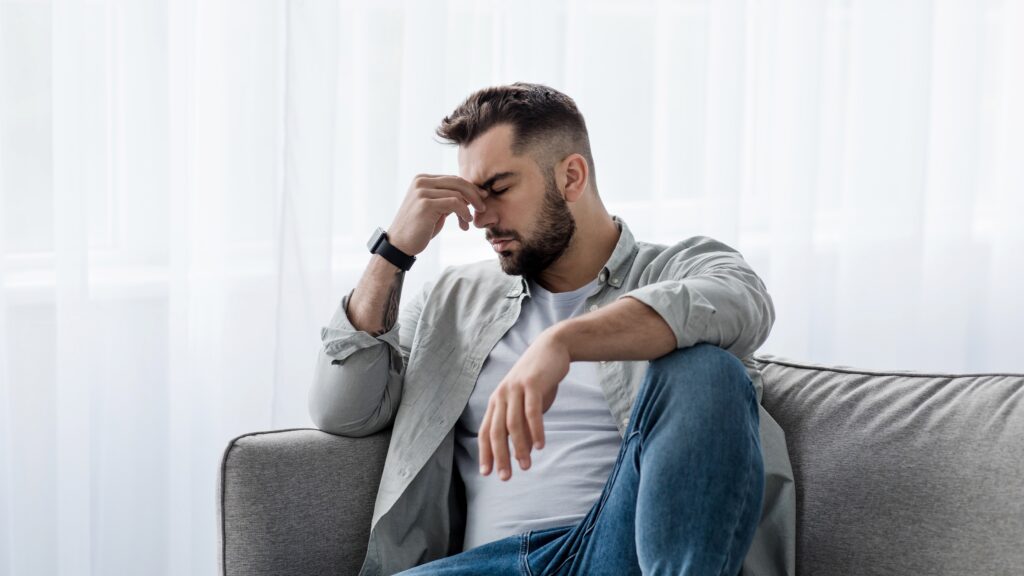 Man sitting on couch with head in hands looking sad.