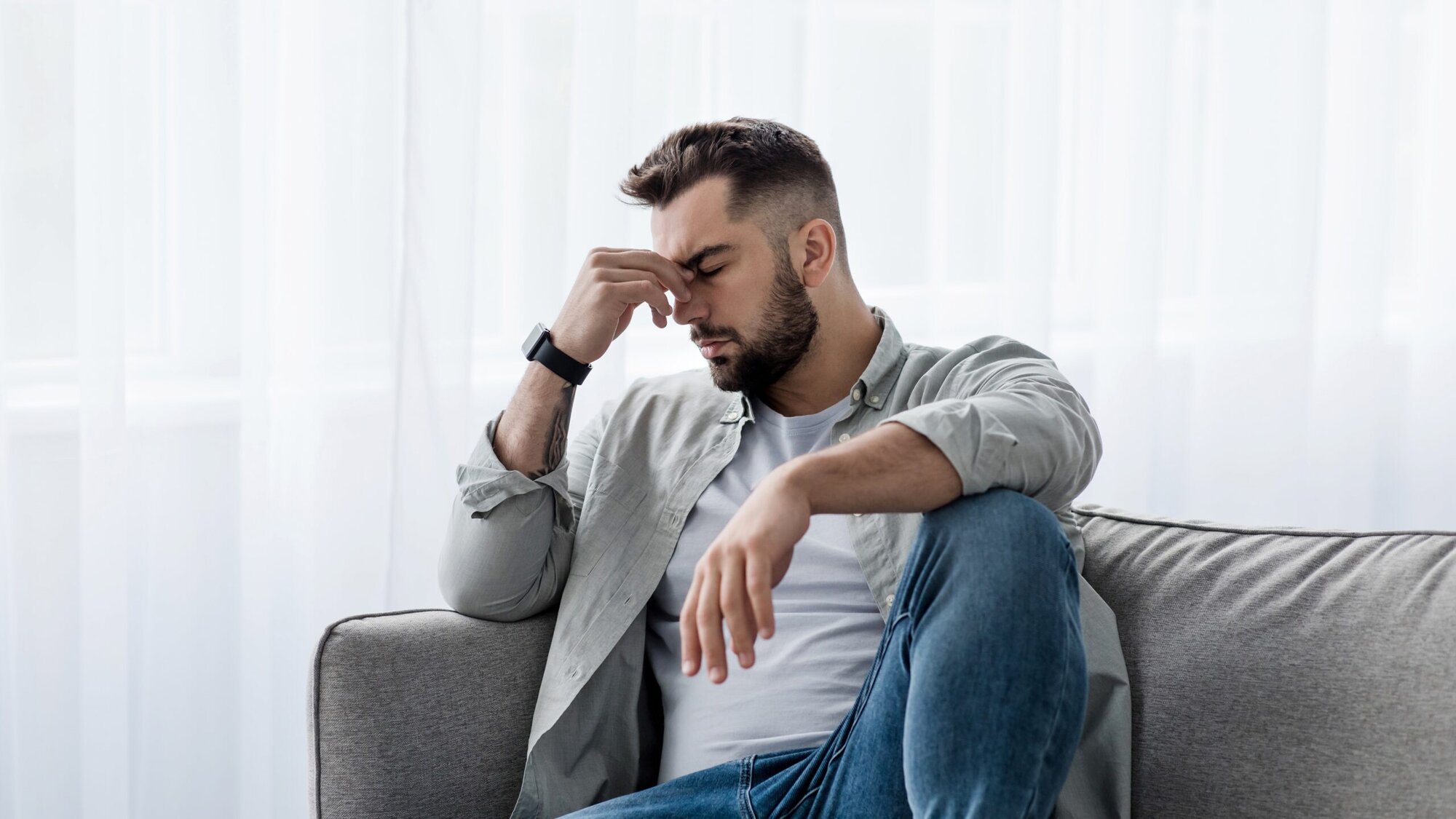 Man sitting on couch with head in hands looking sad.