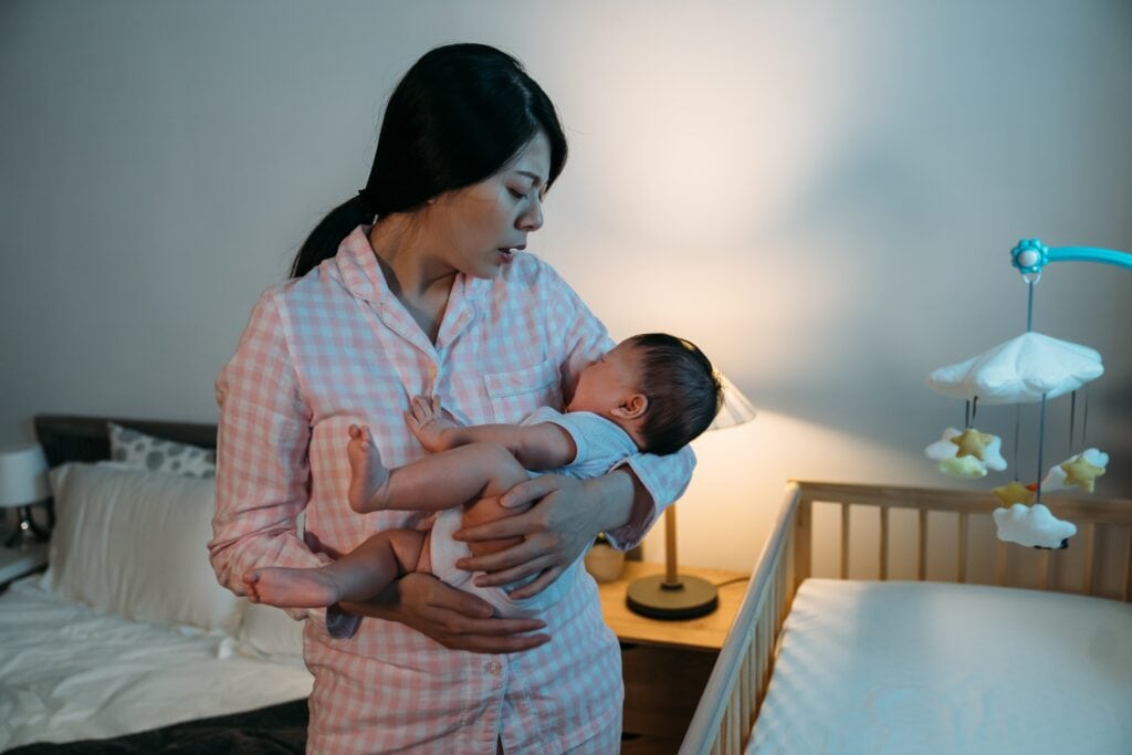Woman holding her baby at night next to the crib.