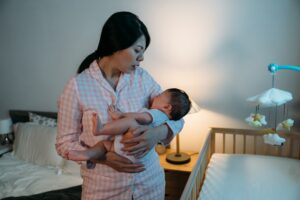 Woman holding her baby at night next to the crib.