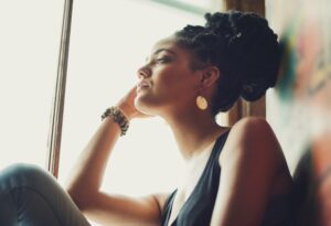Woman sitting against window with head in hand looking out.