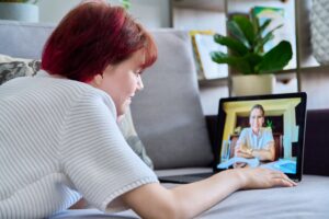Woman laying on couch looking at computer. Therapist is on the computer.