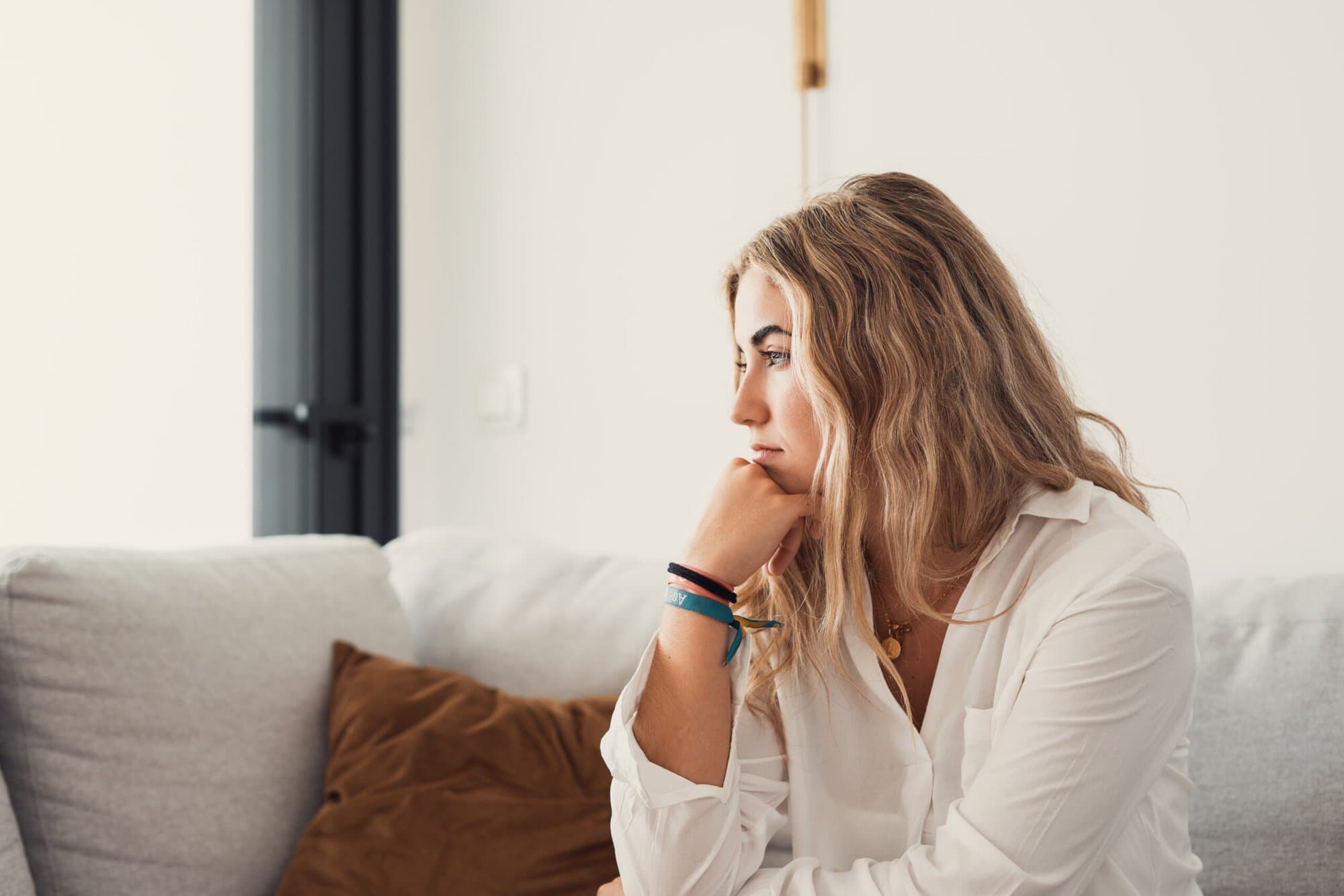 Woman sitting on couch with hand under chin looking to the side.