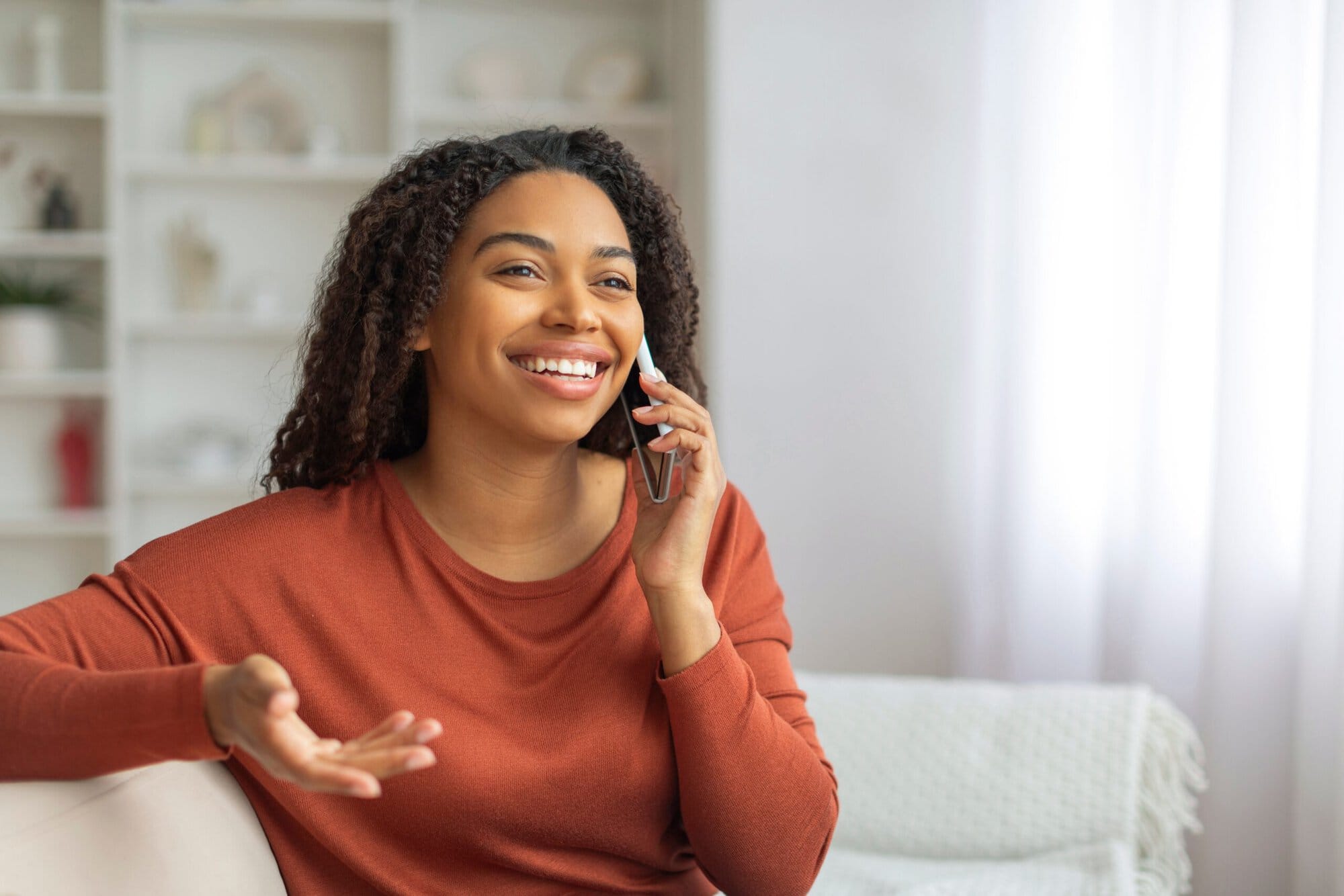 Woman sitting on couch talking on phone smiling